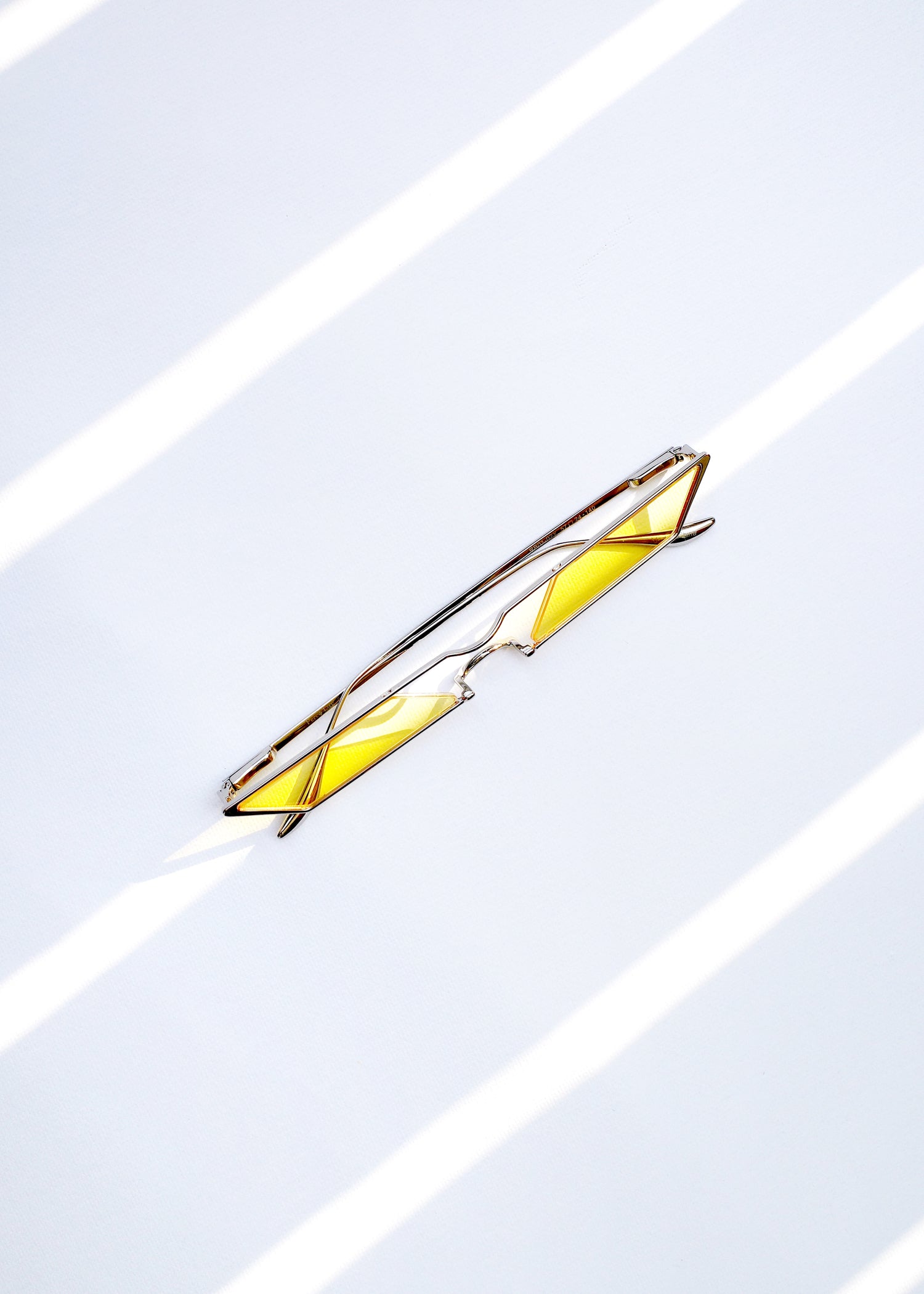 sunglasses with rhombus shaped light yellow lens and silver frames under the sun